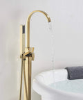 Solid Brass Freestanding Bathtub Faucet With Hand Shower in Gold Polished Finish, next to filled bathtub, water flowing, floor mount