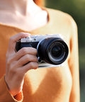 Hand Grip For Fujifilm X M5 Camera With L Shape Bracket Built In Arca Quick Release Plate And Battery Access Anti Slip Microfiber Pad Aluminum Alloy Handle For A Secure Pro Grade Vlog Ready All Day Comfort Grip being held in use outdoors.