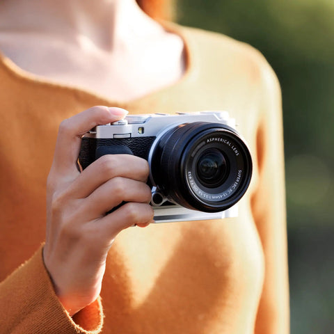 Hand Grip For Fujifilm X M5 Camera With L Shape Bracket Built In Arca Quick Release Plate And Battery Access Anti Slip Microfiber Pad Aluminum Alloy Handle For A Secure Pro Grade Vlog Ready All Day Comfort Grip being held in use outdoors.