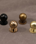 Four round cabinet knobs in black, brass, bronze, and gold finishes on a gray surface.