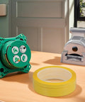Four Pack Yellow Heat Resistant Paper Tape Featuring A Dang Tough Hold on a wooden surface with a grey tape dispenser.