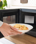 Hand placing food in microwave with 10 Pack Microwave Waveguide Covers Mica Sheets Five Point Nine By Four Point Seven Inches installed.