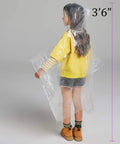 Child wearing clear plastic rain poncho with hat rope, 3'6" tall, from Six Pack Kids Disposable Rain Ponchos Fifty Percent Thicker Emergency Rain Gear Clear Plastic Ponchos With Hat Rope To Keep Heads Dry Durable Yet Lightweight For Outdoor Play And School Trips