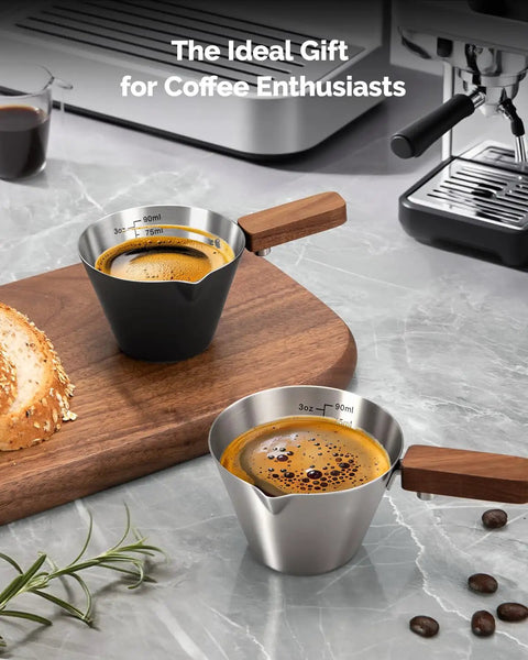 Stainless Steel Espresso Measuring Cup With Wide Mouth And V Shaped Pour Spout, Easy Grip Handle, Built In Scale For Latte Cappuccino Americano Macchiato, Pro Grade For Home Baristas Black on wooden board.