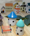 Two Piece Miniature Park Bench Set For Fairy Gardens And Dollhouses in a model village scene with houses.