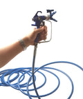 Hand holding a paint spray gun connected to a Badass 50 Foot Airless Paint Spray Hose Built Like A Tank For 8500 Psi High Pressure Handling.