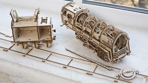 3D Model Steam Locomotive Kit With Tender For Builders And Hobbyists, Gear Driven Train Replica With Rubber Motor, Vintage Steam Era Style For DIY Railfans And Train Nerds. Wooden 3D puzzle locomotive and tender parts on a white table.