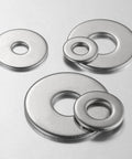 Top-down view of four stainless steel flat washers with centered holes and varying outer diameters.