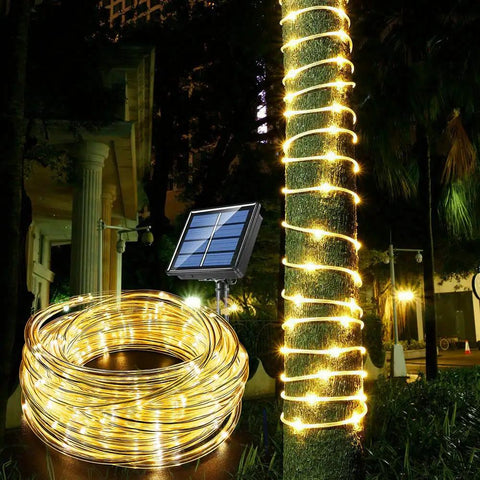 Long 33 Feet Solar Rope Lights With 100 LEDs wrapped around tree trunk, solar panel in garden, warm white glow at night