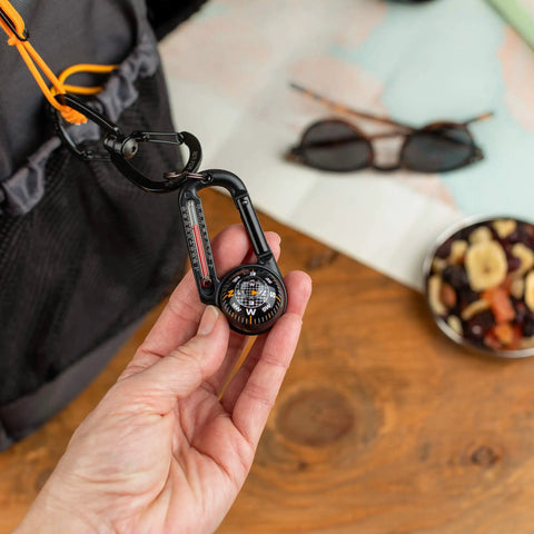 Hand holding Ball Compass And Thermometer Carabiner For Hiking And Camping Clip On Grab And Go Gear For Backpacks Parkas Or Jackets
