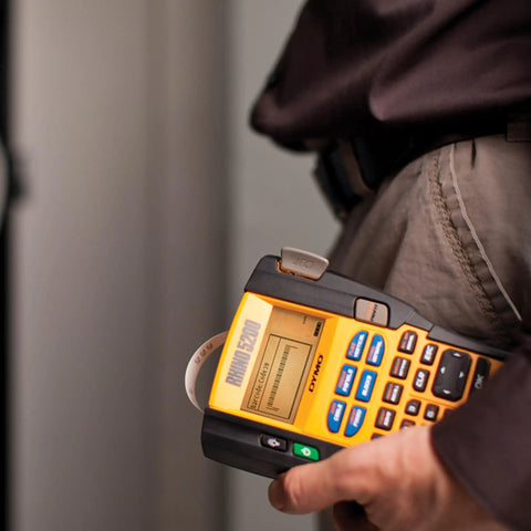 Person using label maker printing Rhino Industrial Flexible Nylon Labels Three Quarters Inch By Eleven Point Five Foot Black Print On White Tape Built Tough For On The Job Moisture And Temperature Resistant Adhesive That Will Not Curl Or Peel Ideal For Harsh Environments