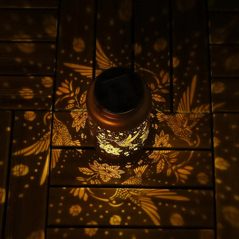 Hummingbird Solar Lanterns For Outdoor Garden Decor projecting warm hummingbird pattern on wooden surface, gold copper finish