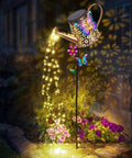 41 Inch Tall Solar Watering Can With LED Lights Garden Stake illuminating flowers at night with butterfly and flower accents