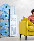 Heavy Duty Steel 5 Gallon Water Jug Rack Space Saving Water Bottle Holder Stand beside yellow couch and water dispenser