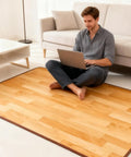 Cozy Imitation Wood Heated Floor Mat With Adjustable Temperature And 12 Hour Timer, Electric Carpet For Home Office Or Yoga, 39 By 59 Inches, Radiant Floor Heating Pad in a living room setting with a person using a laptop.