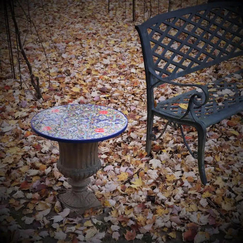 Mosaic outdoor table and metal bench surrounded by autumn leaves on the ground.