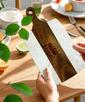 Cutting board with white marble panels and brown acacia wood center stripe, circular handle cutout.