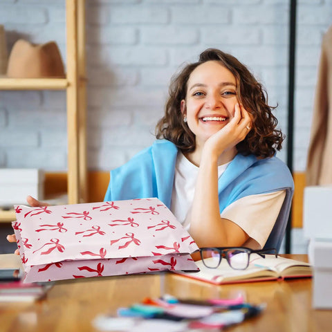 Woman holding 10x13 Inch Poly Mailers 50 Pack Self Seal Shipping Bags with pink bow design, ideal for clothes and small biz