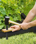 Man using hammer to drive 16 Inch Heavy Duty Rebar Stakes Set Of 16 Ground Anchors With Chisel Point for landscaping timber support.