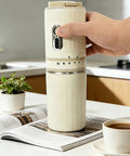 Portable Travel Coffee Maker With Built In Grinder 16 Oz Brew Cup One Touch Manual Drip Brewer held in hand near a potted plant.