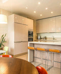 Modern kitchen with wooden table, bar stools at island, pendant lighting, and sleek cabinetry, showcasing contemporary design.