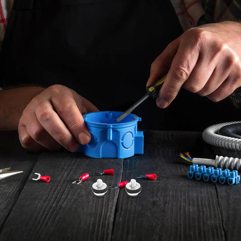 Person assembling electrical components with a blue junction box and various connectors on a wooden table