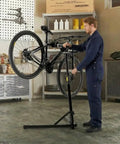 Mechanic using Heavy Duty Bike Repair Stand With Hand Crank Mechanical Lift, Max 110 Lbs Load, Aluminum Work Stand For E Bikes