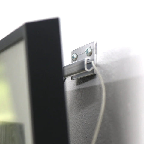 Close-up of Badass Heavy Duty Picture Hangers With Tough Aluminum Grip securely supporting a black frame on a wall.