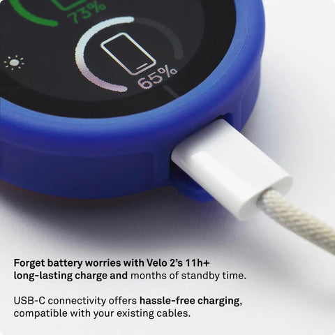 Close-up of Velo 2 Bike GPS Computer With Wireless Global Navigation, blue casing, USB charging cable connected, 65% charge displayed.