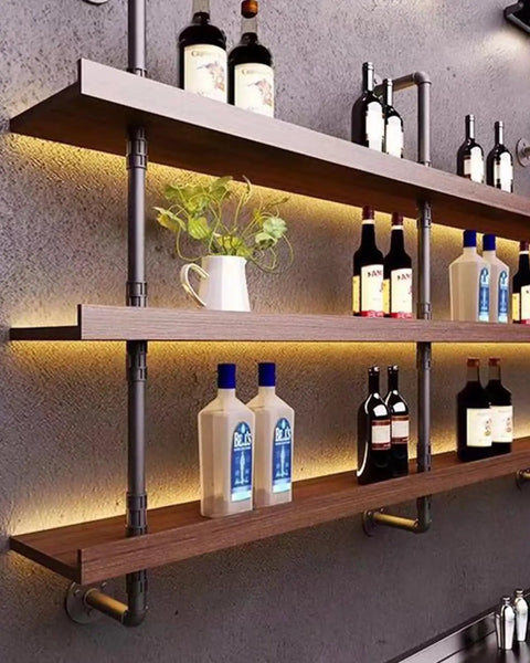 Industrial shelving using Heavy Duty One Half Inch Cast Iron Floor Flange Fittings For DIY Furniture And Shelving Projects Black DN15 Pipe Connections 4 Pack Pre Drilled Holes For Quick Install with pipes supporting wooden shelves holding bottles and plants against a gray wall.
