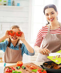 Montessori kids kitchen knife set with wooden handles on a bright kitchen counter; child holds two tomatoes at cutting board.