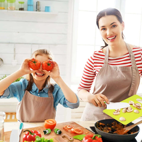 Montessori kids kitchen knife set with wooden handles on a bright kitchen counter; child holds two tomatoes at cutting board.