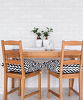 Dining area with wooden table and chairs, white brick wall, decorative plants, and chevron-patterned cushions on the chairs