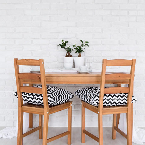 Dining area with wooden table and chairs, white brick wall, decorative plants, and chevron-patterned cushions on the chairs