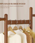 Close-up of Freestanding Walnut Wood Coat Rack With Wheels, displaying solid wood texture and four hanging garments.