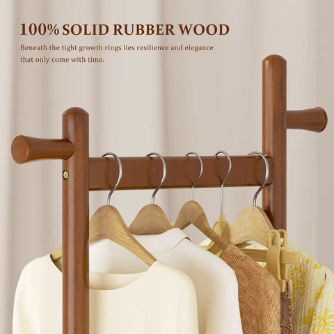 Close-up of Freestanding Walnut Wood Coat Rack With Wheels, displaying solid wood texture and four hanging garments.