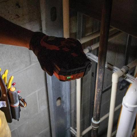 Rechargeable LED Work Light With 1000 Lumens, Magnetic Mount in a hand, used in a jobsite with visible pipes and tools.