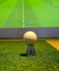 Golf ball on black plastic tee with simulator in background, part of Indoor Golf Spot Light For Simulators And Practice kit