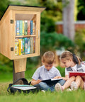 Outdoor Library Book Box With Double Shelf For Book Swapping And Sharing Weatherproof Little Library Cabinet With Shatterproof Clear Door Easy Mount DIY Wooden Storage For Neighborhoods And Schools installed outdoors with children reading nearby.