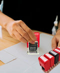 Hand using Slick Adjustable Received Date Stamp For Offices And Businesses Straight Up Reliable Two Color Ink With Blue Text And Bold Red Dates Easy To Reset Up To Thirteen Consecutive Years Built Tough For Daily Mailroom Hustles And Quick Paperwork Sign Offs on a document.