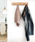 Slick Modern Wall Mounted Coat Rack In Brushed Brass With Heavy Duty Hooks For Entryway living room or kitchen holding striped towel and jeans.
