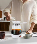 Person using Glass Turkish Coffee Maker Portable 600ml Electric Turkish Pot for Turkish coffee in a kitchen setting.