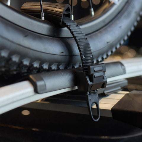 8 Piece Cradle Ratchet Strap Kit for bike racks close-up, securing a bicycle wheel on a roof carrier rack, black strap detail