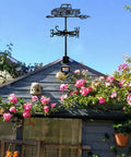 Black Metal Pickup Truck Weathervane Ornament on shed with pink flowers in garden; Outdoor Yard Decor Wind Direction Indicator