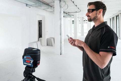 Pro Level 12V Green Beam Cross Line Laser With 100 Foot Reach And Smart Visimax Tech used by an operator controlling the device with a smartphone.