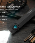 ArkPro EDC Flat Flashlight Rechargeable USB C Pocket Light With 1500 Lumen Flood, black with blue button on wooden surface