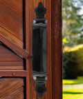 Black Decorative Six Inch Pressed Steel Gate Handle with Seven Sixteenth Inch Hex Head Mounting Screws for Wood Gates Easy to Install and Rust Resistant Gate Hardware on wooden gate outdoors.