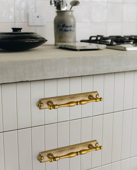 Gotta Have These Antique Brass Cabinet Pulls 2 Pack Featuring Classic Turned Spindle Shape And Chunky Decorative Backplate on a white tiled kitchen drawer.