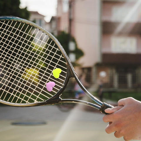 Tennis racket with Heart Shaped Tennis Dampeners Set Of 4 Silicone Vibration Absorbers in yellow and purple on strings