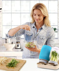 Woman using All In One Sprouting Jar Kit With 2 Wide Mouth Mason Jars Mesh Lids Blackout Sleeves Stand And Tray For Easy Home Sprouting Of Fresh Broccoli Bean And Alfalfa Sprouts In Just Days, preparing salad in kitchen.